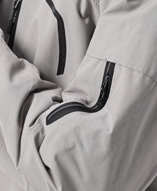 Close-up of the khaki jacket's drawstring hood, high collar, zippered chest pocket and zippered sleeve pocket