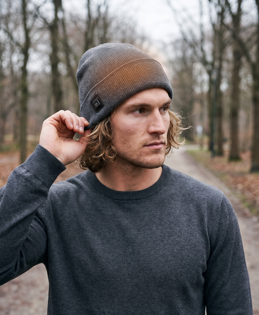 Men's gray heated beanie with the USB cable and smart switch coiled beside it, lifestyle photo