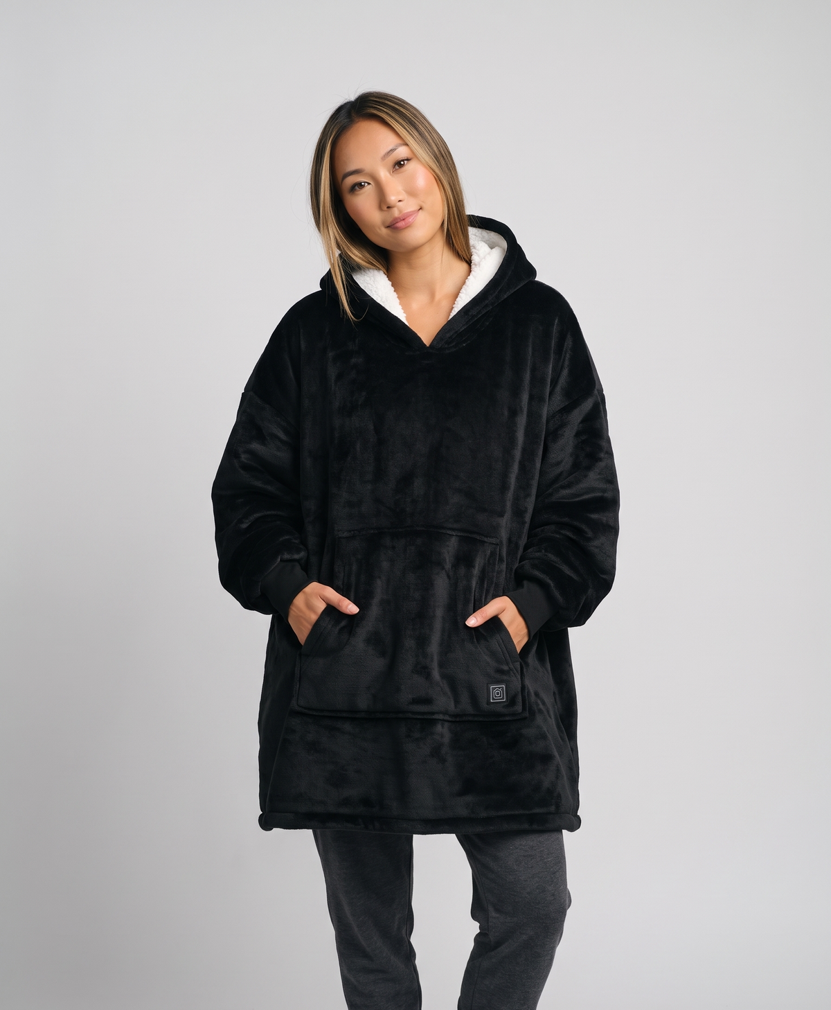 Woman in a black heated wearable blanket hoodie with white sherpa hood, studio portrait