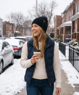 Woman in a black heated knit beanie on a snowy sidewalk with coffee, candid photo