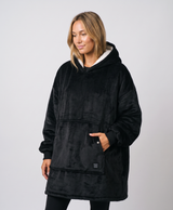 Woman wearing an oversized black heated blanket hoodie with raised arms against a plain light background