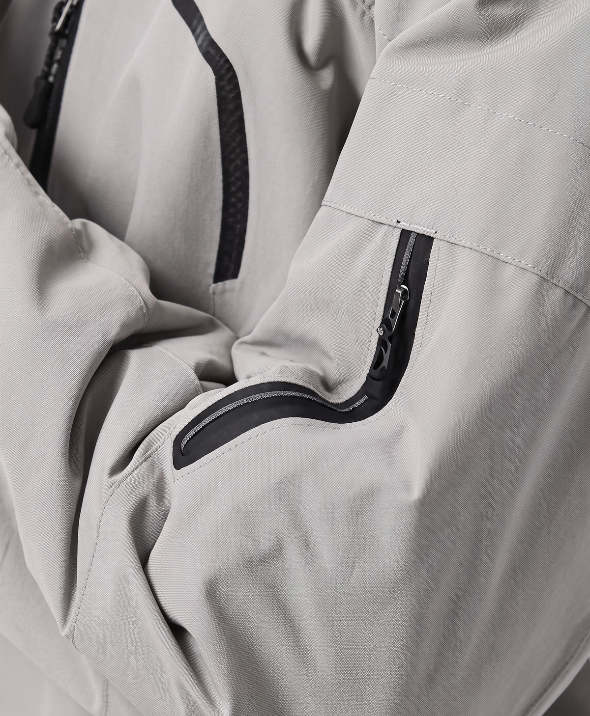 Close-up of the khaki jacket's drawstring hood, high collar, zippered chest pocket and zippered sleeve pocket