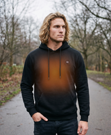 Man in the black heated hoodie holding a power bank beside the front pocket, with the chest power button visible