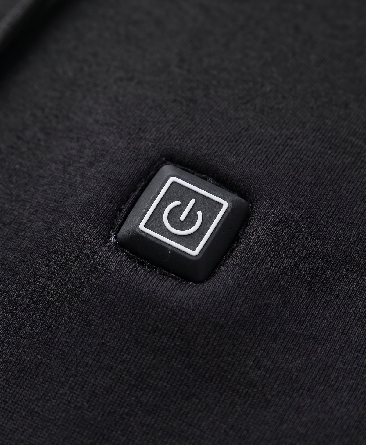 Close-up of the black heated hoodie's chest power button patch, hood drawstrings and metal-tipped cords