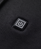 Close-up of the black heated hoodie's chest power button patch, hood drawstrings and metal-tipped cords