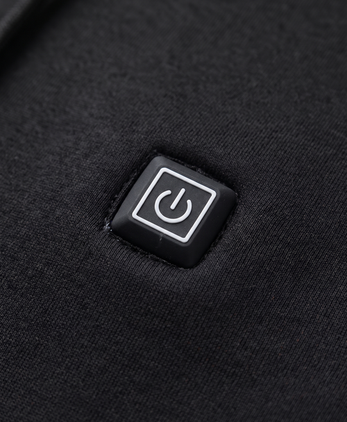 Close-up of the black heated hoodie's chest power button patch, hood drawstrings and metal-tipped cords