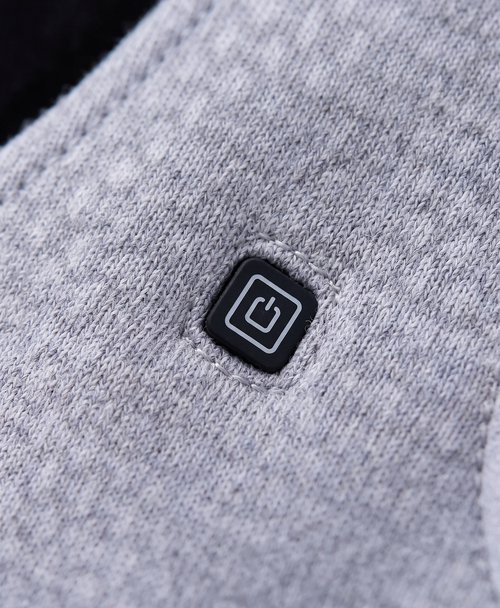 Close-up of the heated vest's chest power button on the diamond-quilted gray fabric