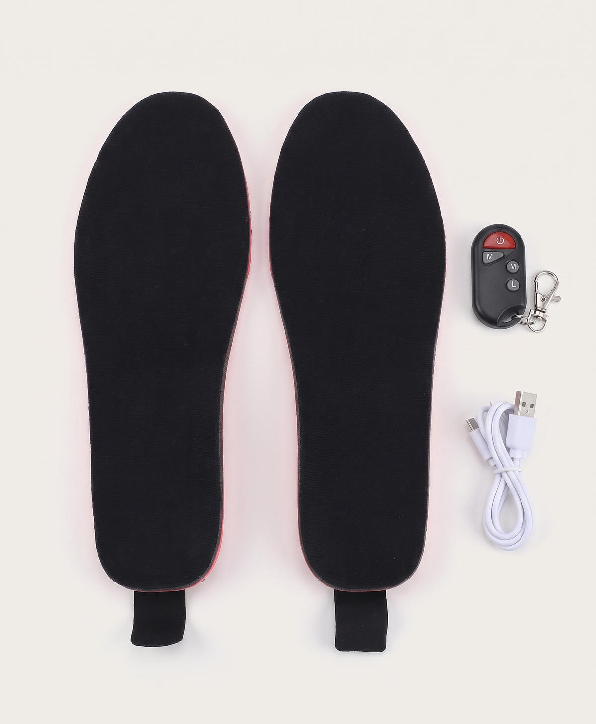 Black heated insoles with the wireless remote control and white charging cable on a white background