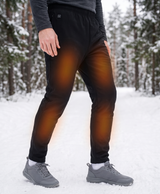 Man in black heated pants and sneakers standing in a snowy mountain setting, with heat level graphic