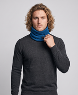 Man wearing a blue fleece heated neck gaiter, studio-style photo showing the front power button and snowy background