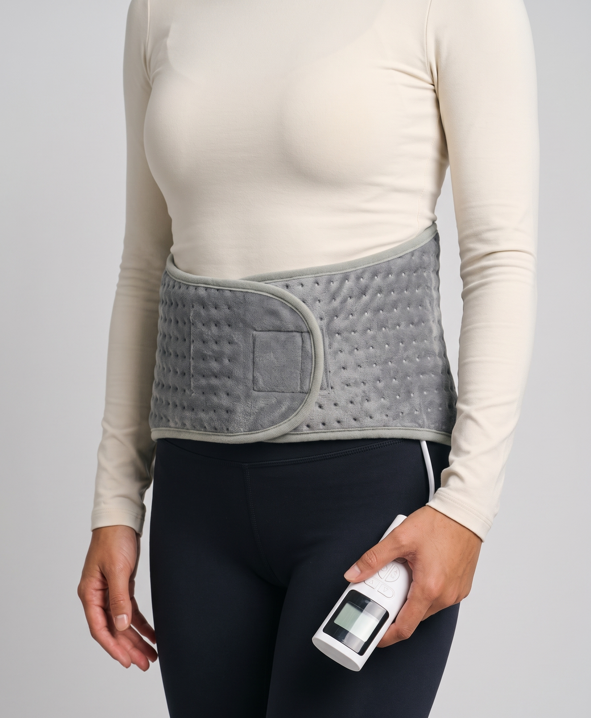 Woman seen from behind wearing the silver gray heated waist belt over a white tee, heating zone glowing across the lower back