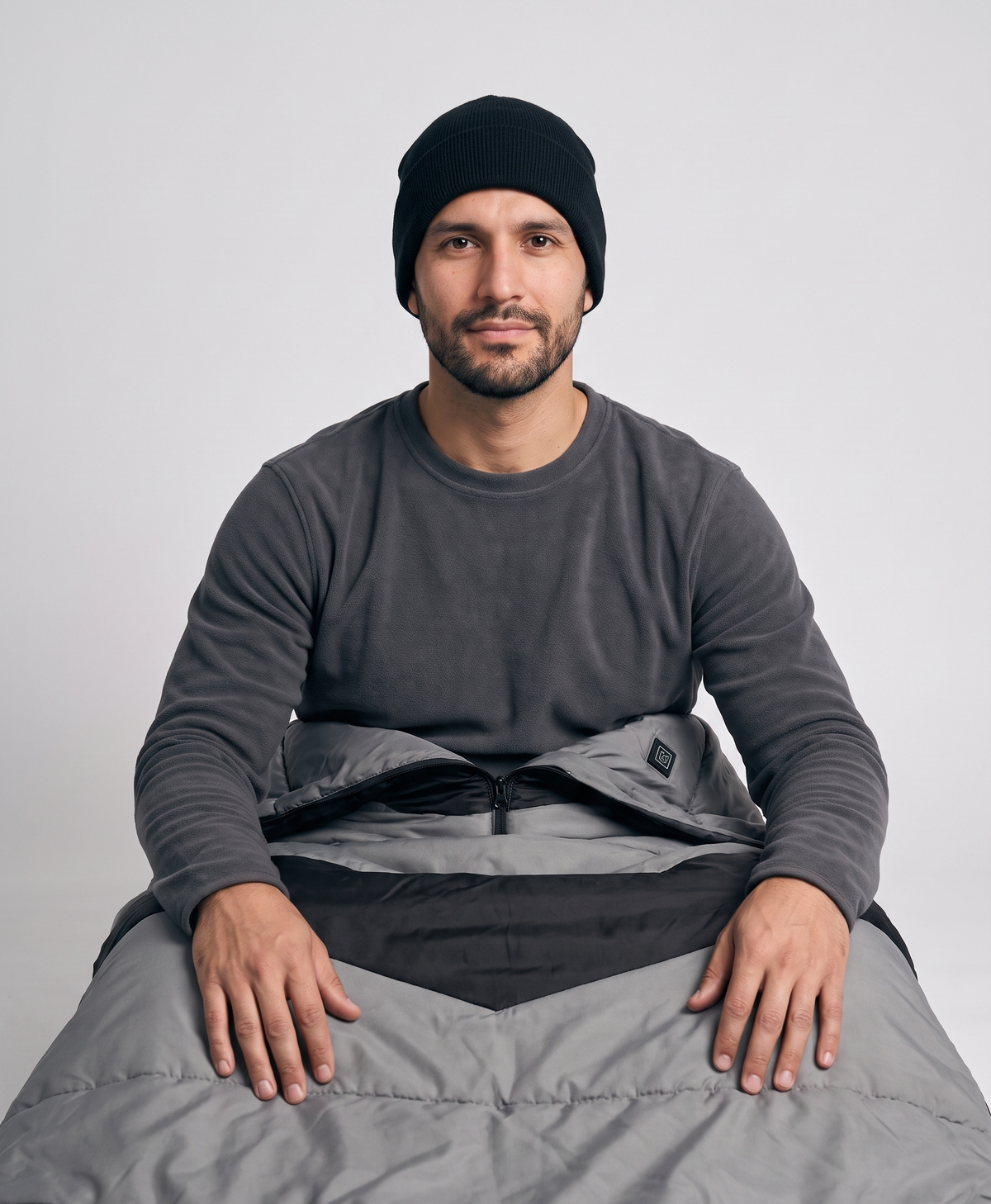 Gray and black heated sleeping bag laid flat beside a black compression sack with straps, on a white background