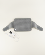 Gray heated waist belt wrapped at the waist with its hook-and-loop strap, held next to the digital controller showing level 9