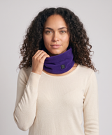 Woman wearing the purple fleece heated neck gaiter, pointing to the power button on the band, studio-style photo